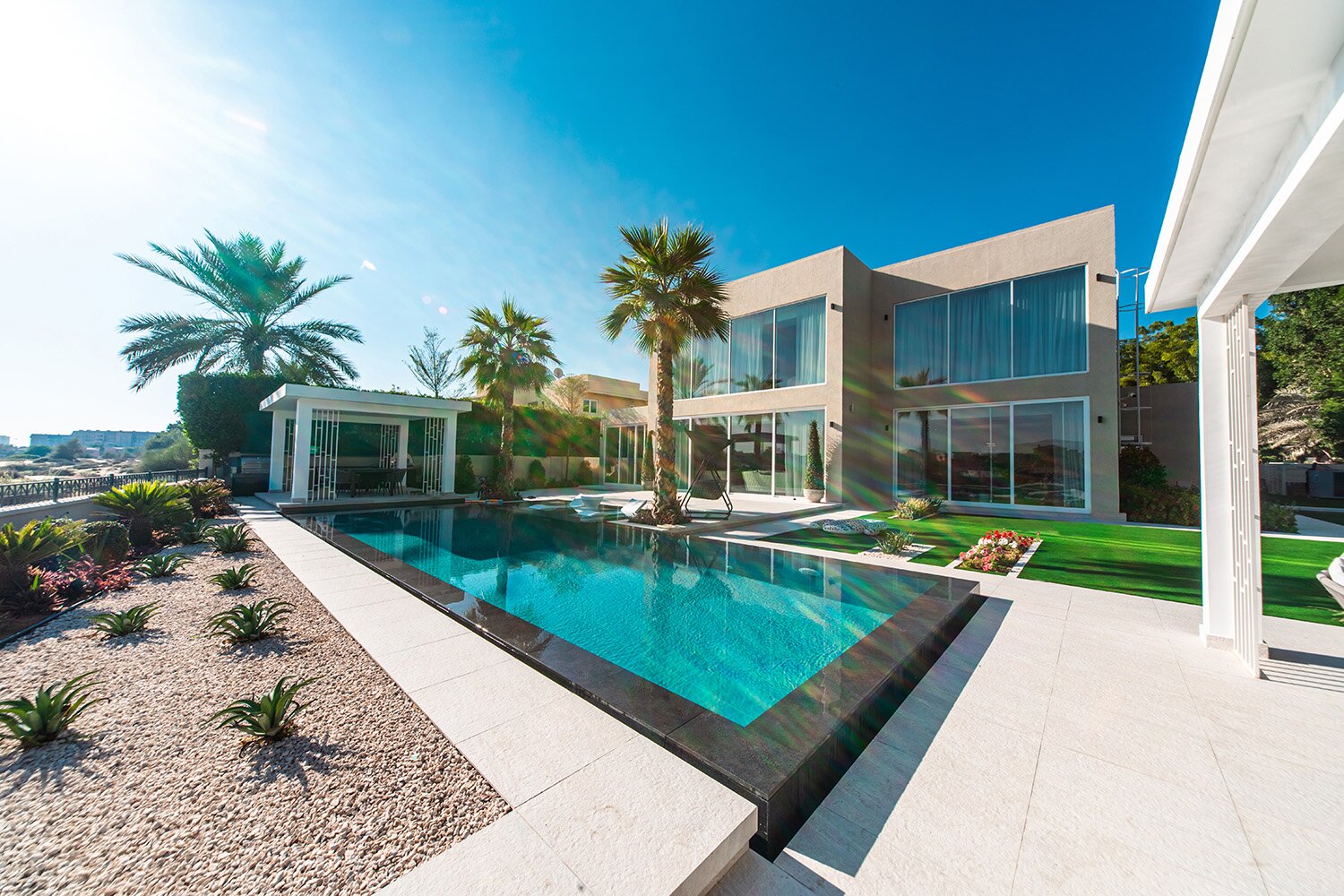 Luxury villa landscaping Dubai with beachfront pool, palm trees, and desert-adapted garden beds.